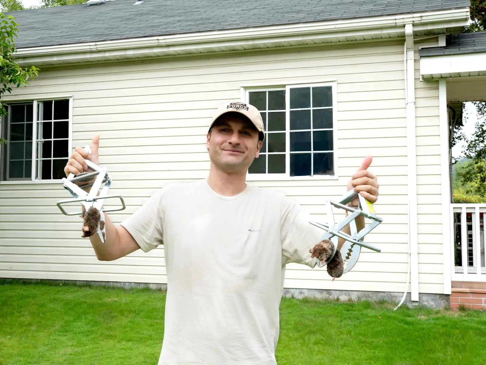 A man holding reusable mole traps in front of a house has a big smile on his face
